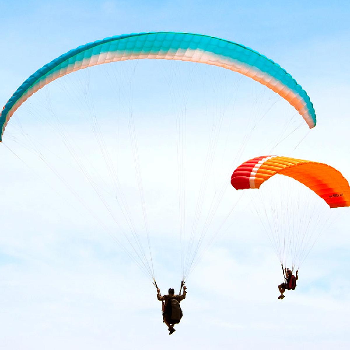 Two people paragliding. One is using a teal parasail. The other parasail is two toned orange.