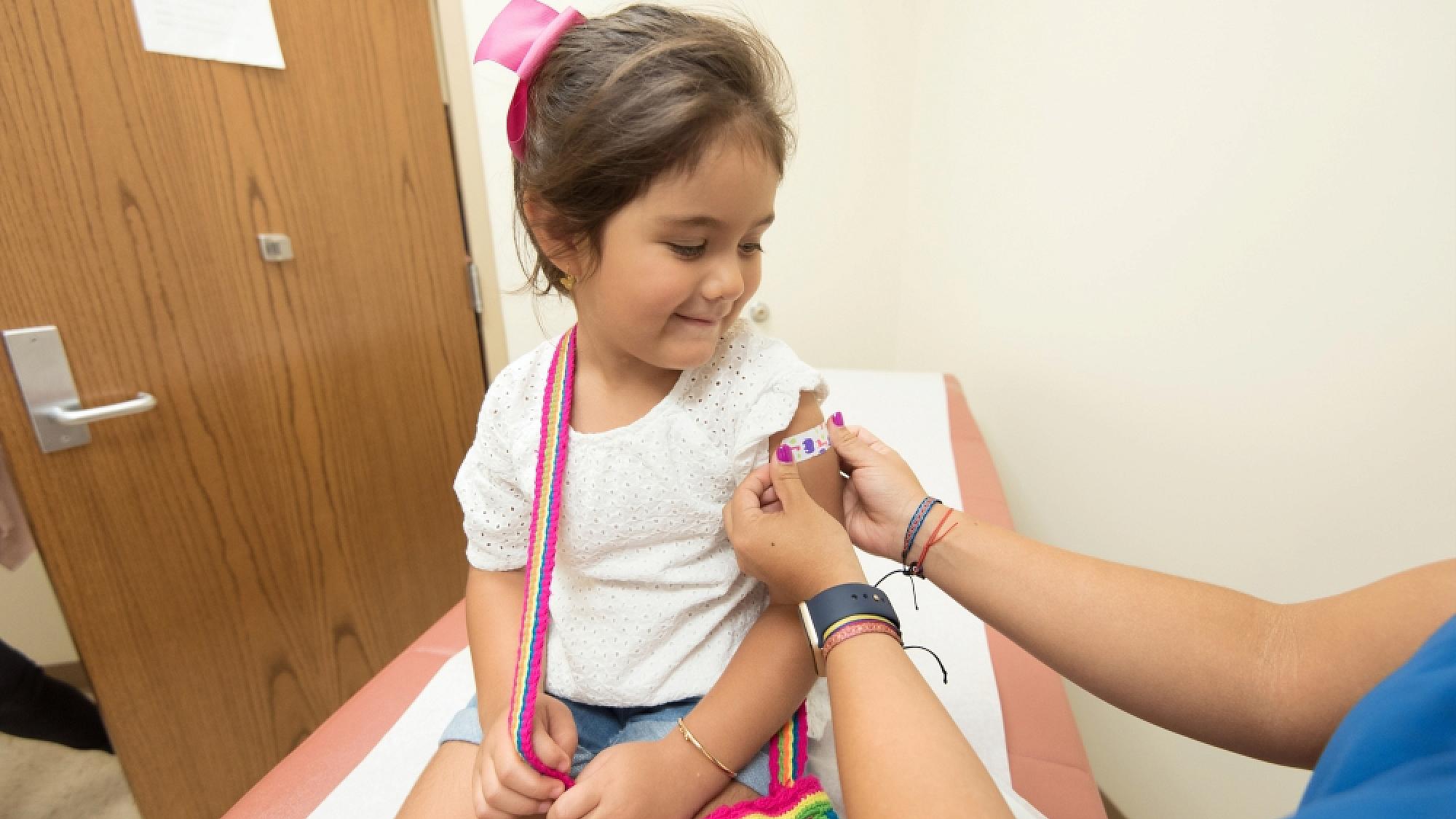 A child receives a band-aid from a nurse, beside the UofU Health logo