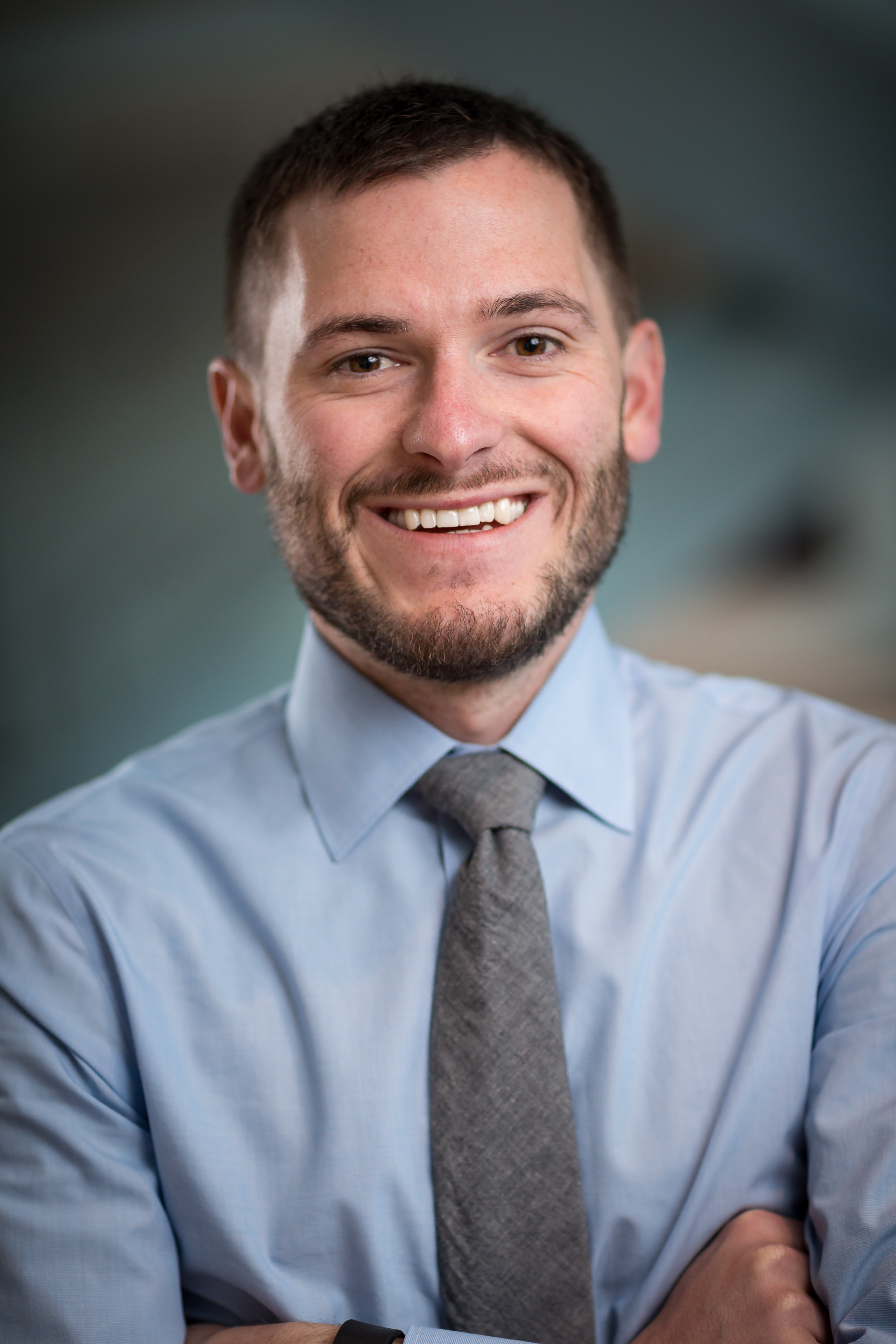 Profile photo of a smiling man in a blue collared shirt and tie.