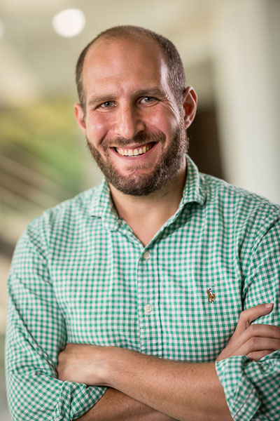 Profile photo of a person in a green collared shirt grinning at the camera.