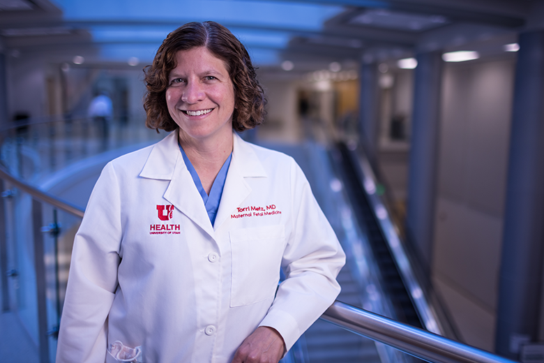 Torri Metz wearing a white coat standing in the hallway of a hospital. She has short wavy brown hair.