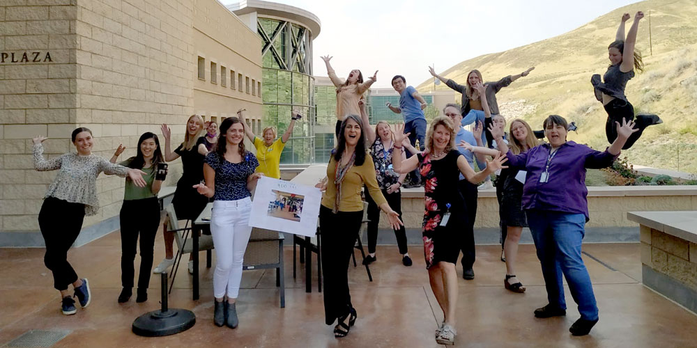 Ulrich Group waving their hands and jumping in the air on the Research South Patio of Huntsman Cancer Institute