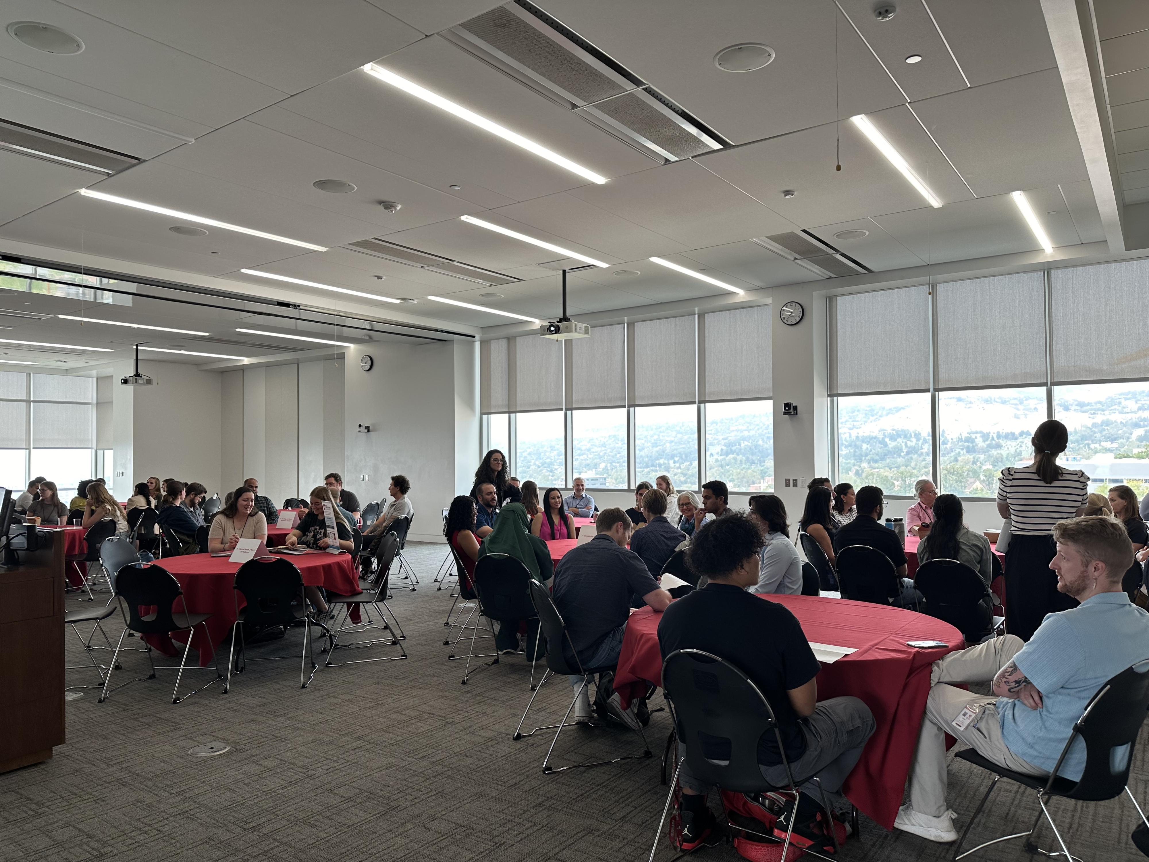 Students, faculty, and staff gather around discussion tables.