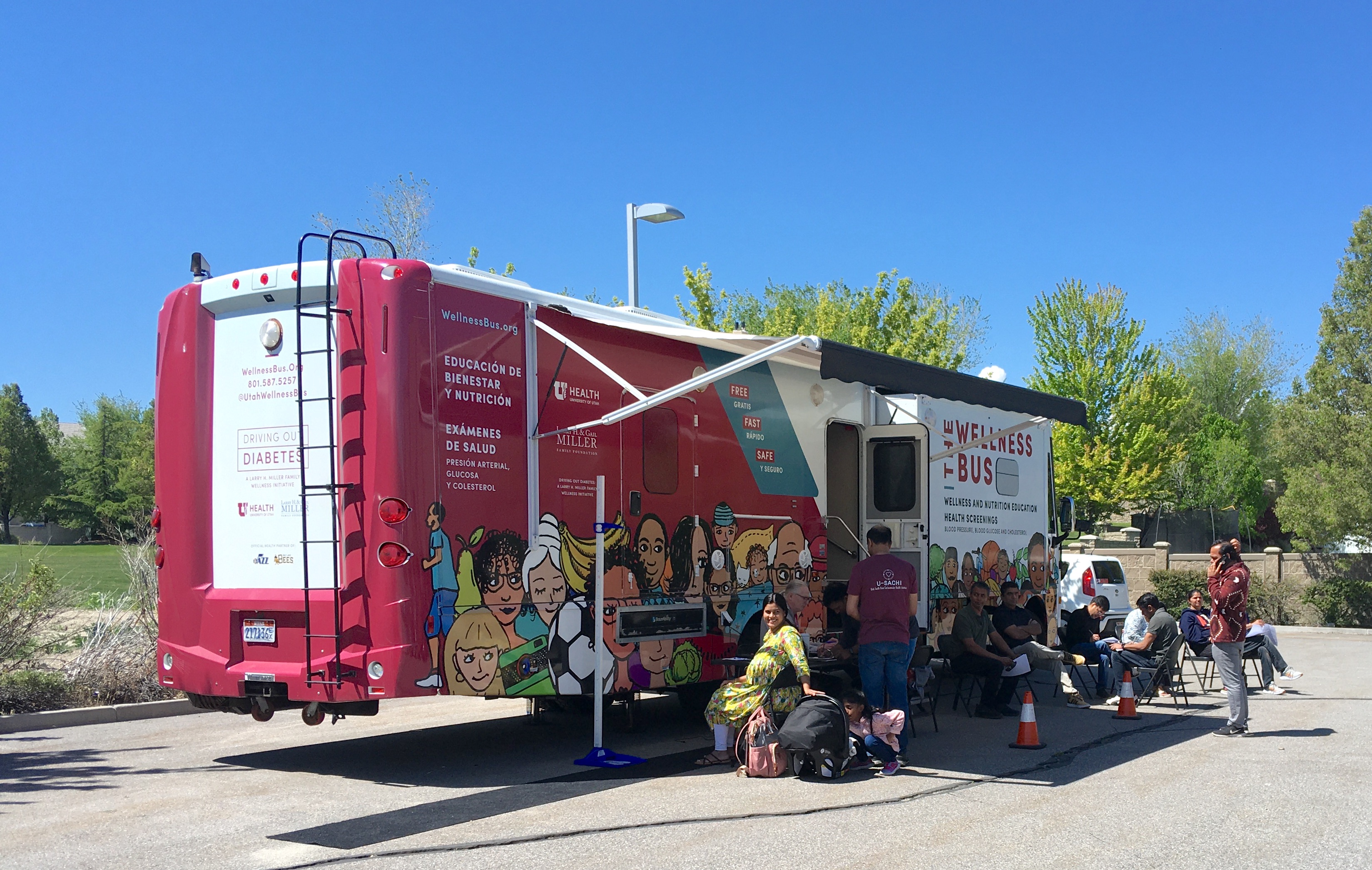 Ten people outside the Wellness Bus, a mobile health center set up in a sunny parking lot.