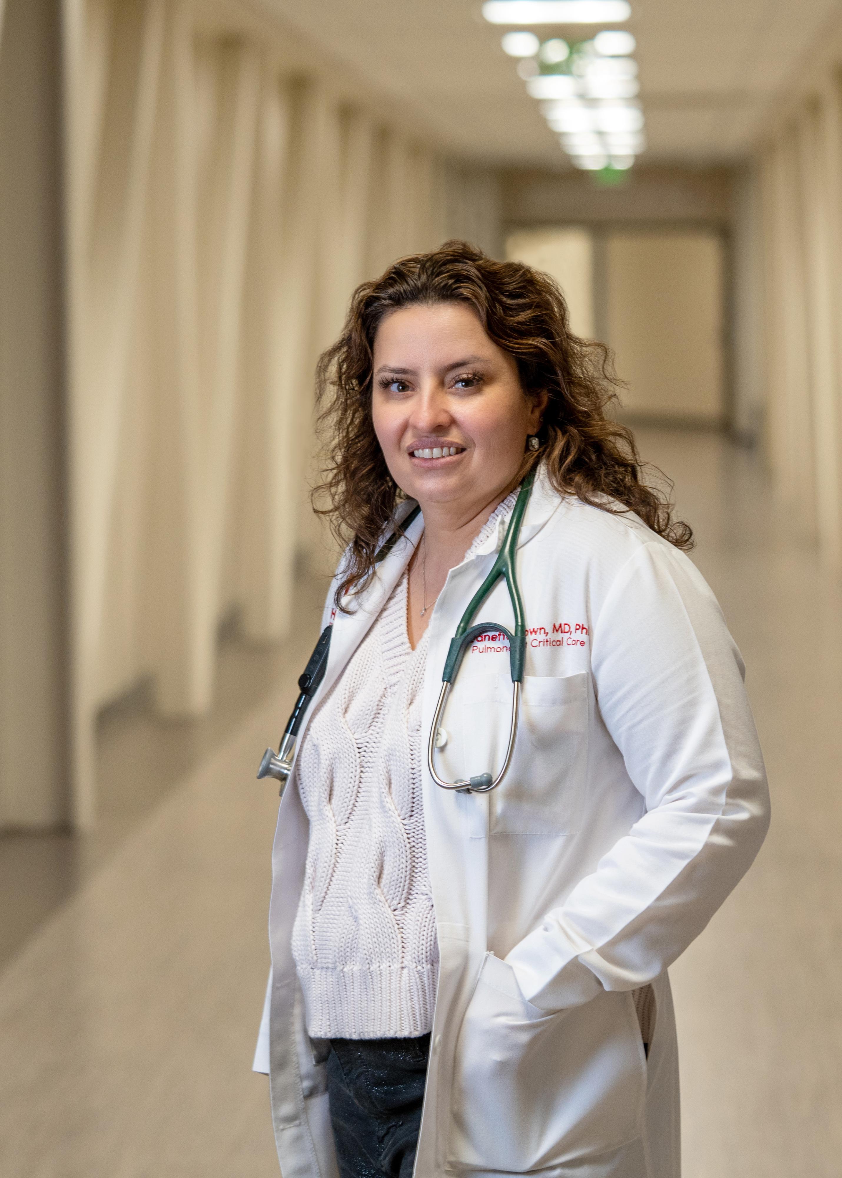 A woman in a white coat stands in a long hallway.