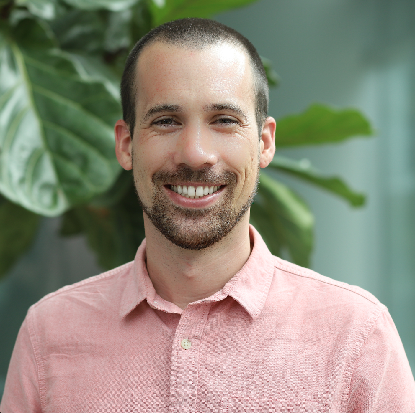 Smiling person in a peach button-up in front of a tree.