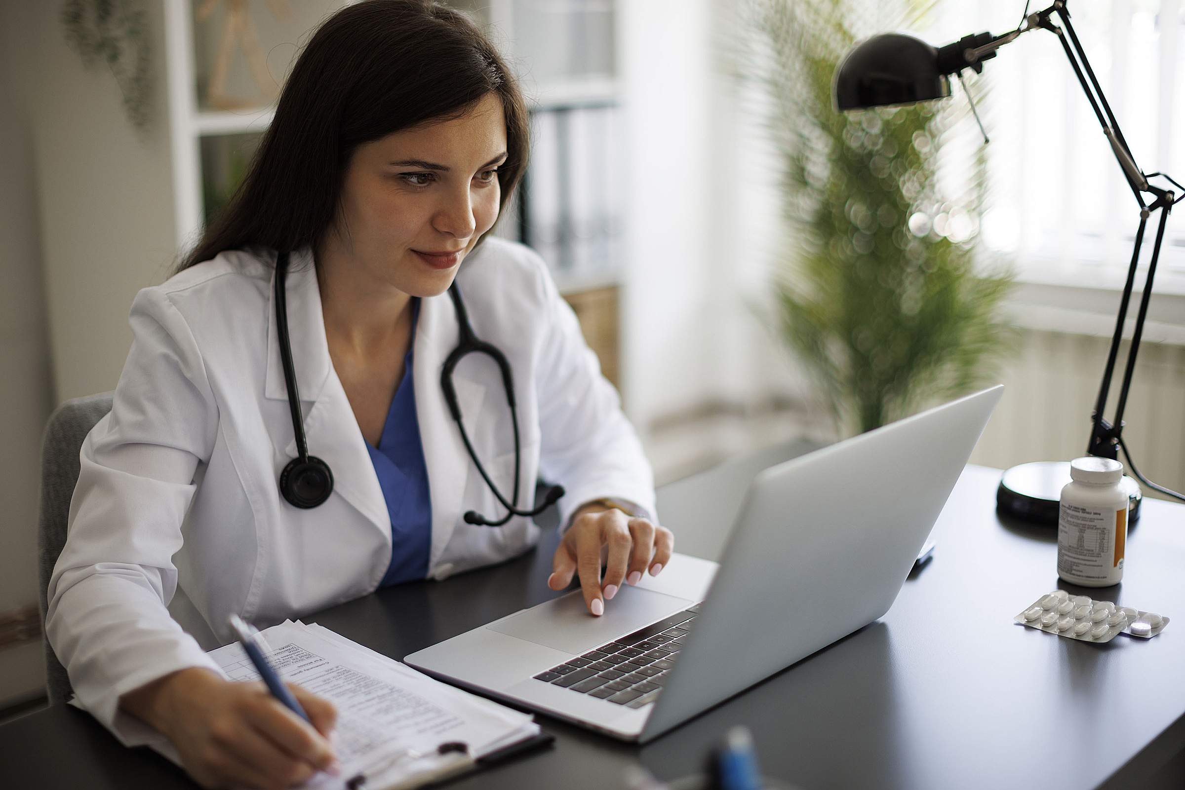 A doctor in a white coat scrolls on a laptop.