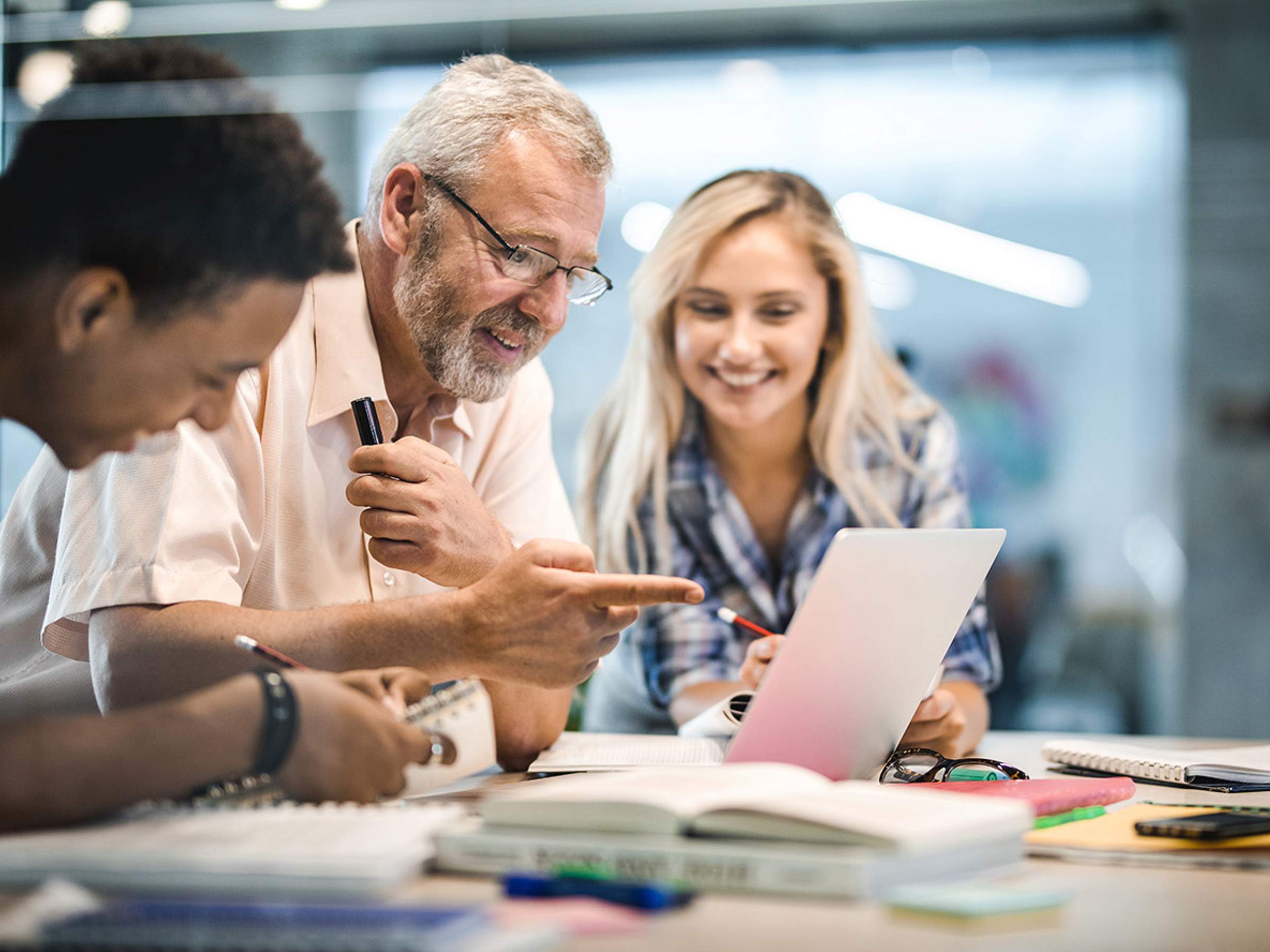  two students with teacher in classroom looking at laptop