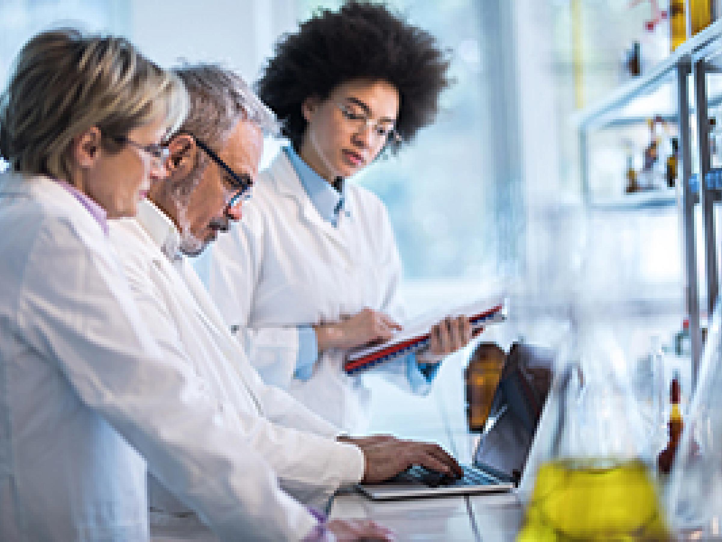 3 researchers in white coats standing at a counter in a lab