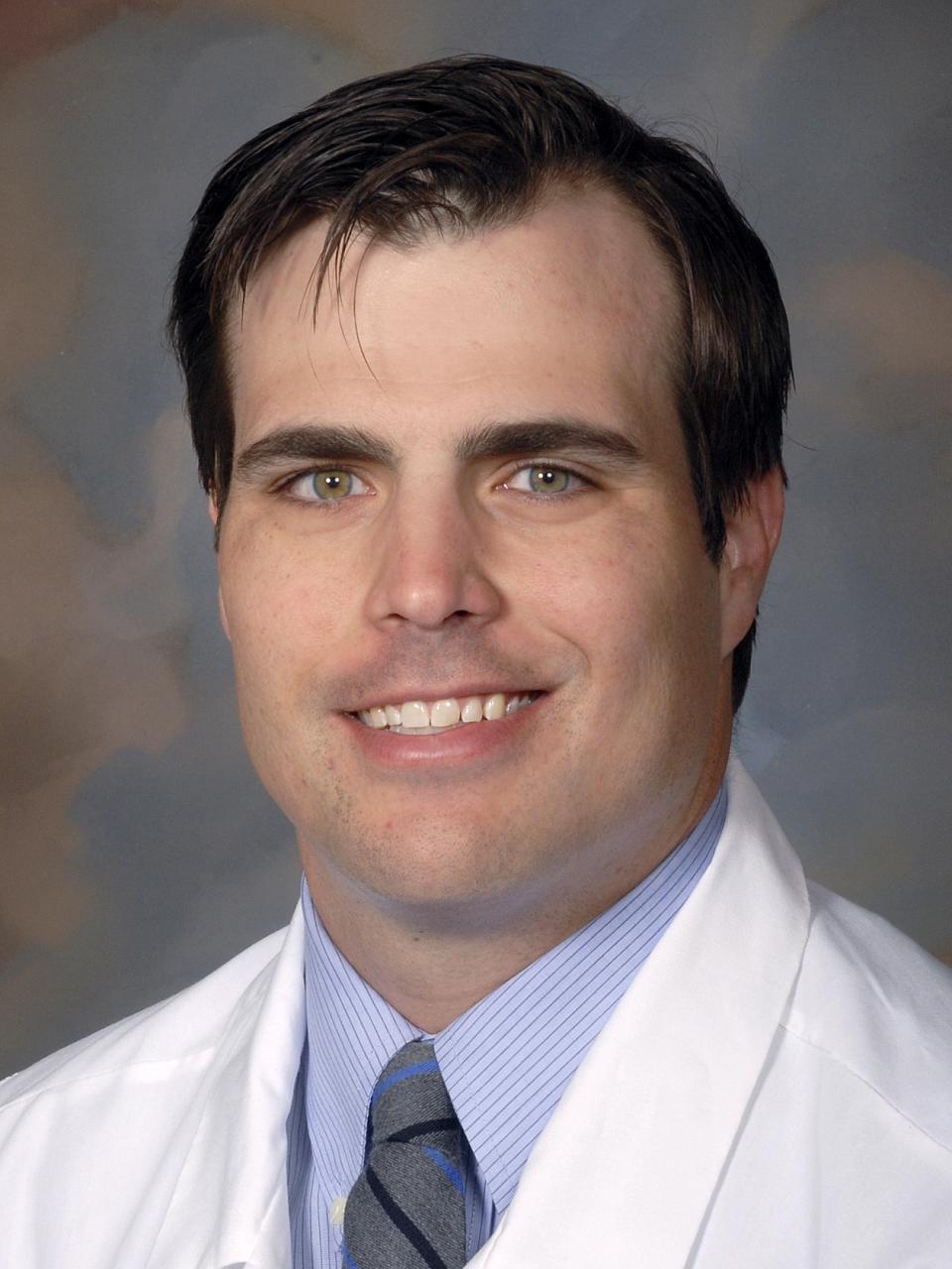 A man with short, dark hair in a white medical coat.