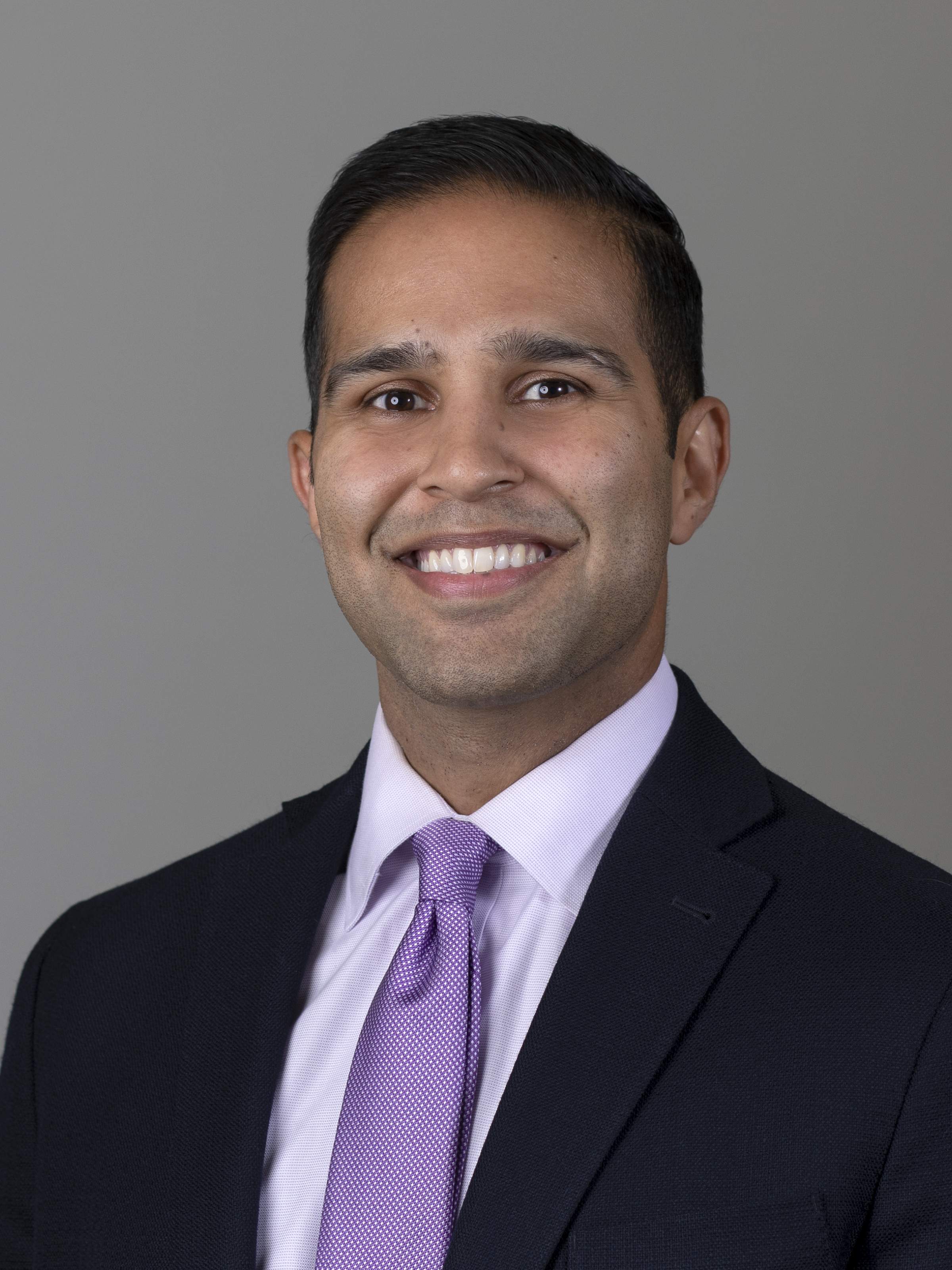 Profile photo of a man in a suit smiling at the camera.