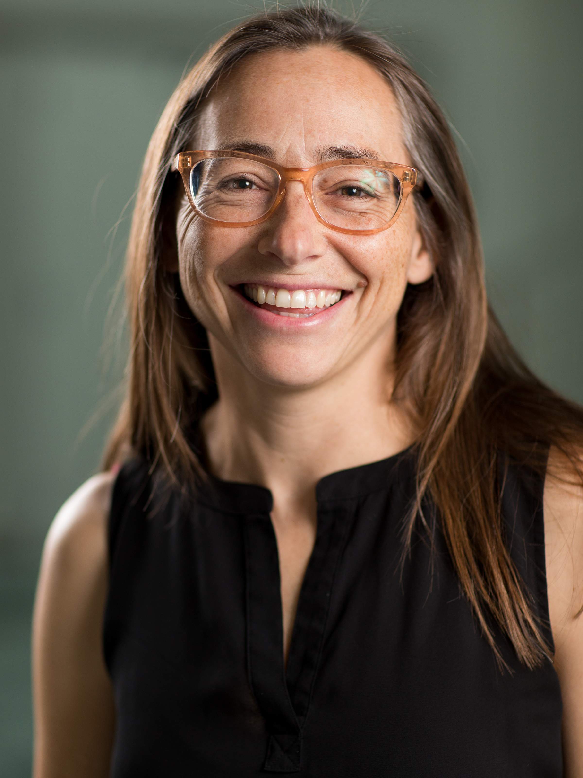 Profile photo of a woman wearing a black shirt and orange glasses, smiling at the camera.