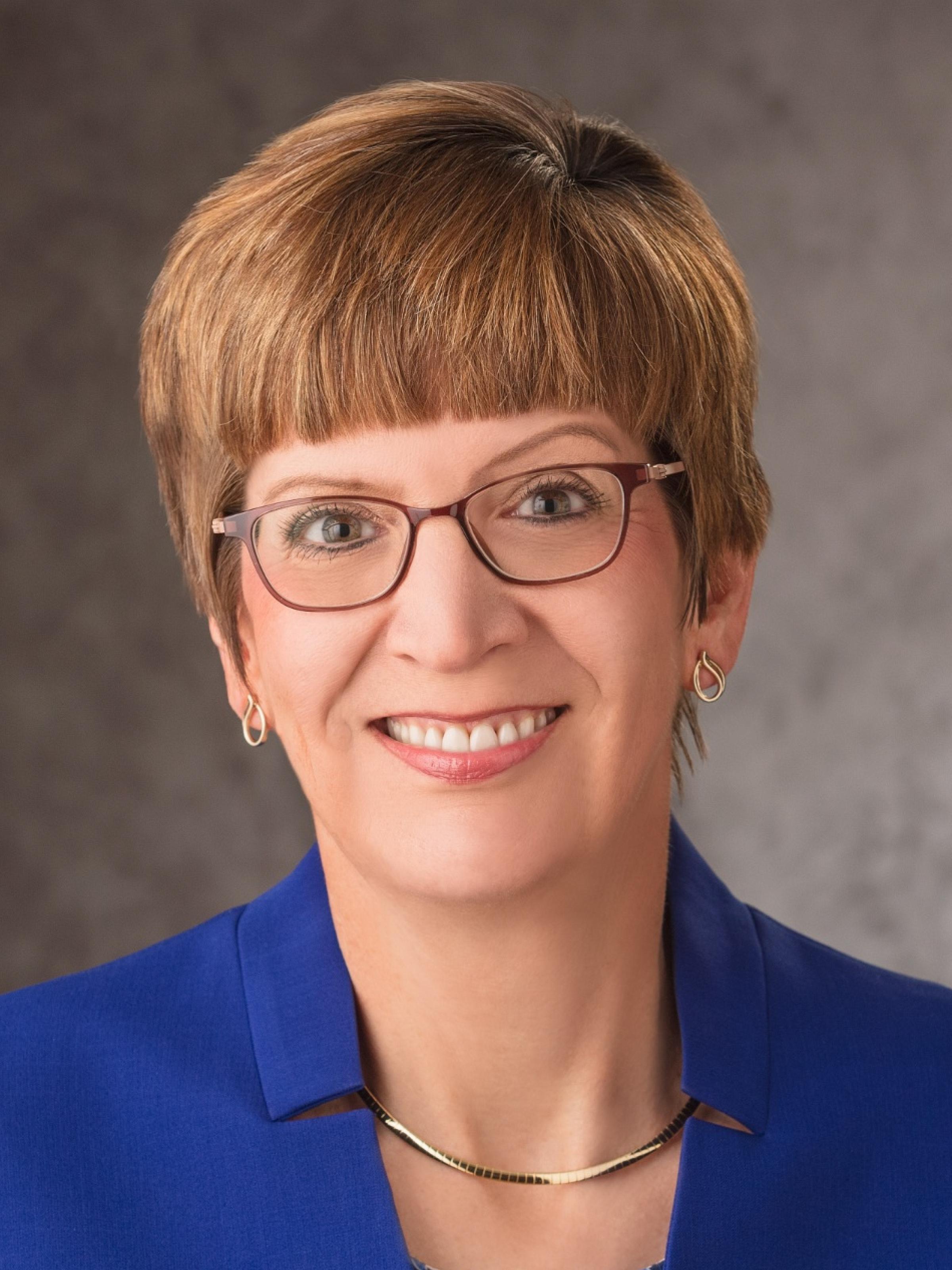 portrait of Marla J. De Jong smiling in a blazer and glasses