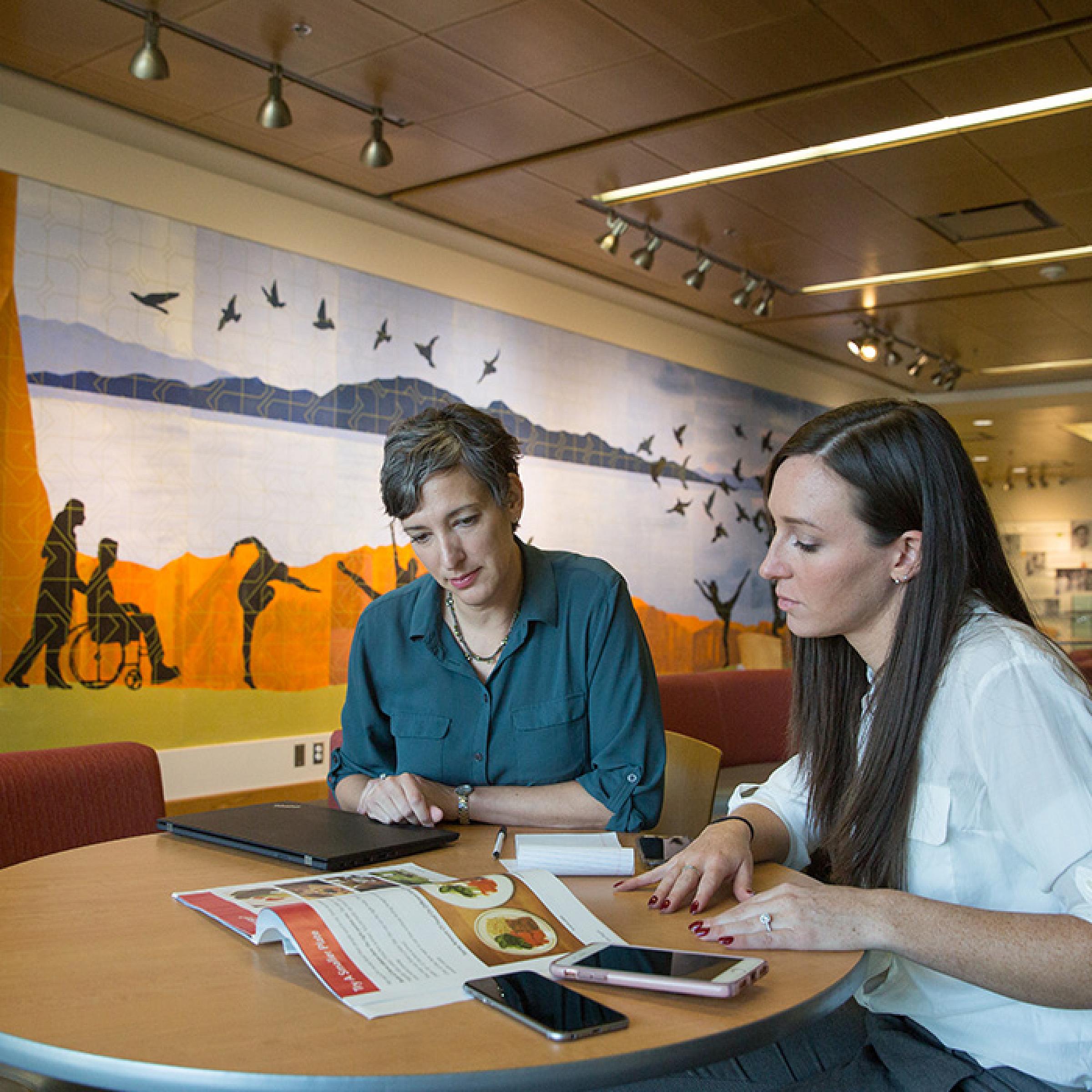 Two People Sitting at Table Reading with Mural Background