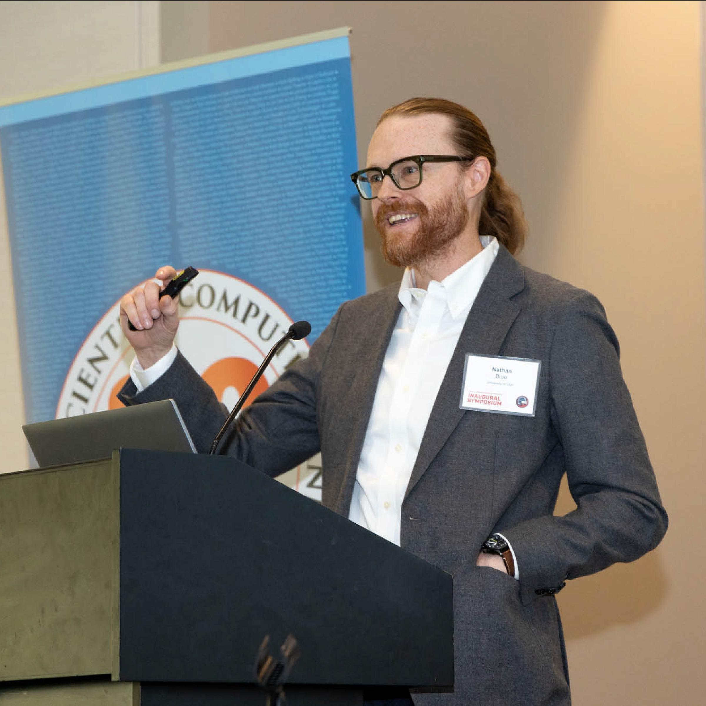 A man with red hair speaks behind a podium.