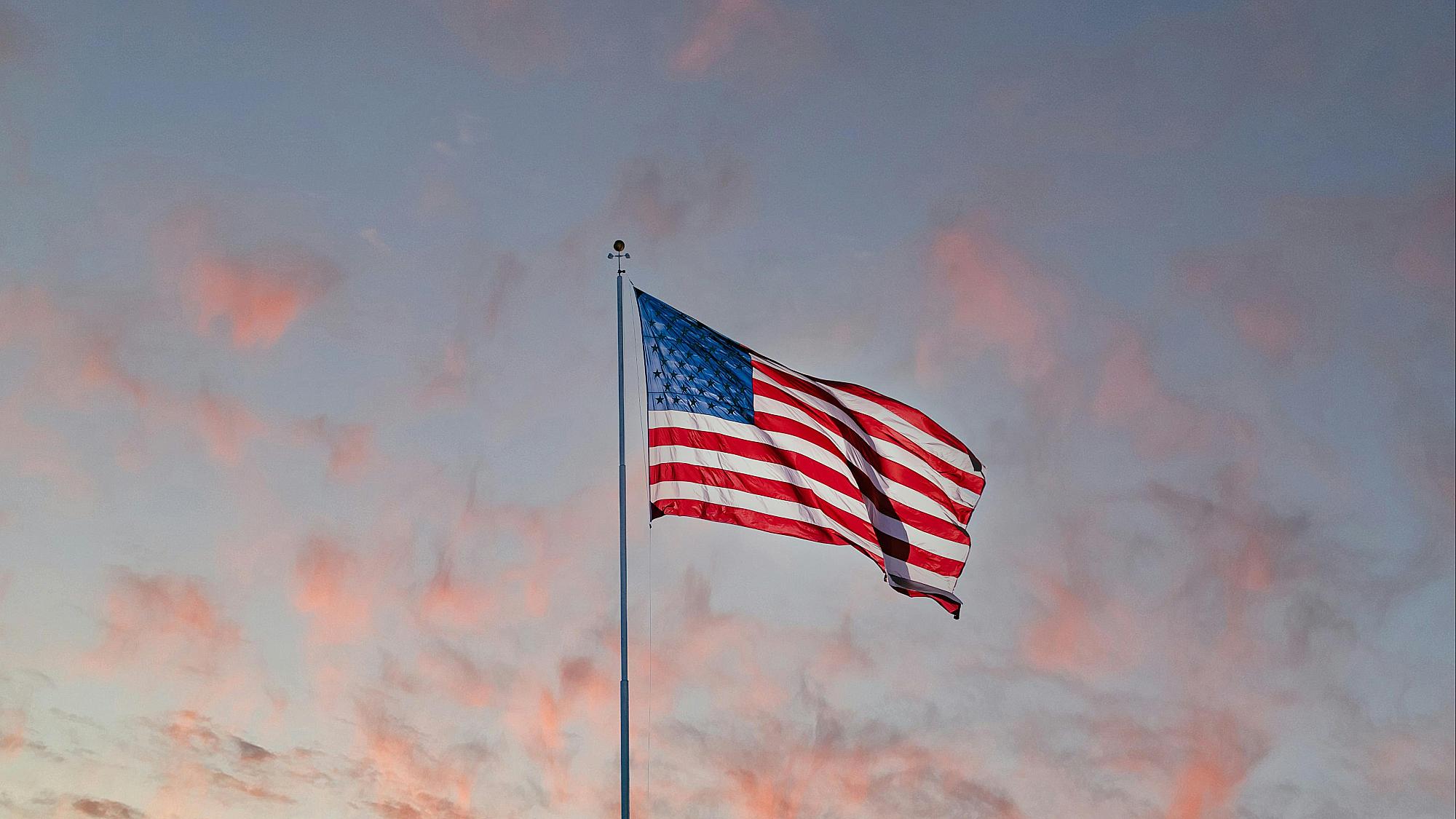 the United States' flag unfurled on a flagpole with a twilight sky in the background