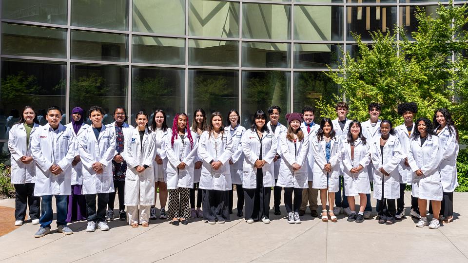 the 2023 PathMaker Scholars cohort smiles while wearing their white coats outside of the Huntsman Cancer Institute