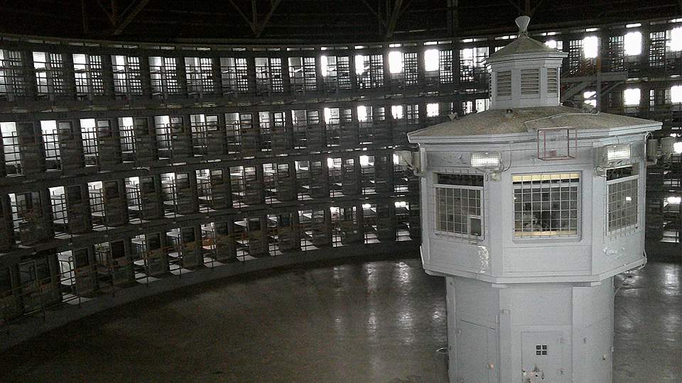 Black-and-white photo of the interior of a prison. A guard tower in the middle of an atrium has line of sight into every cell. External link: (https://attheu.utah.edu/health-medicine/a-new-look-at-the-stateville-prison-malaria-experiments/)